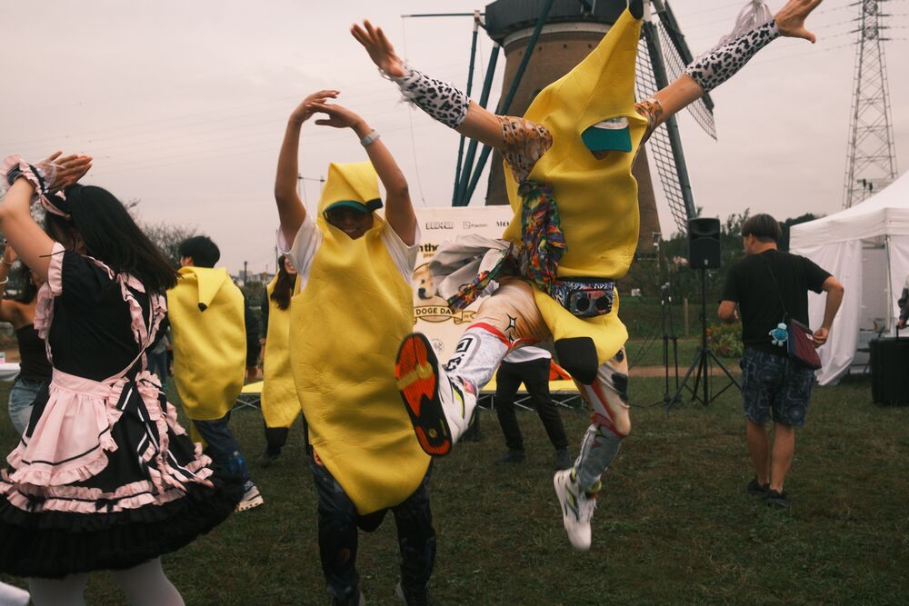 A banana-costumed fan leaping mid-dance on the grass as a maid-costumed dancer and others move around